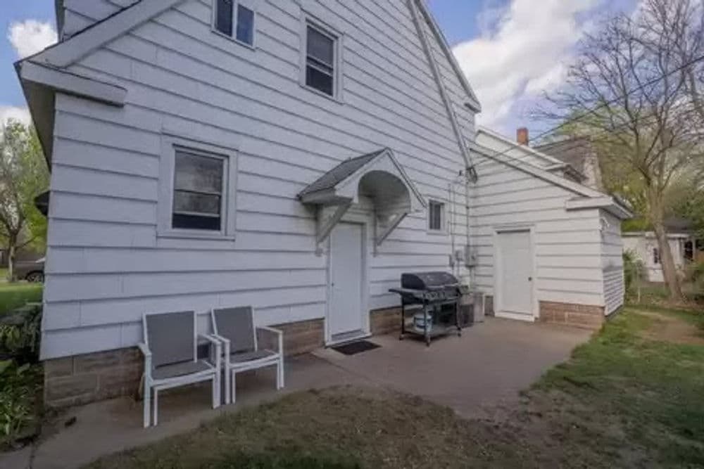 Exterior view of a white two-story house with a patio, grill, and seating area.