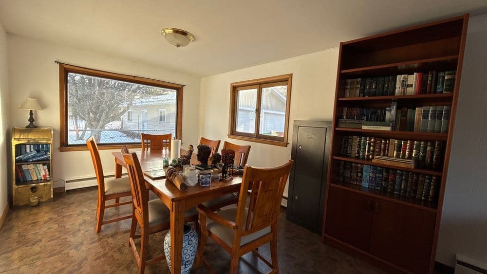 Cozy dining area with wooden table, chairs, bookshelves, and natural light from large window.