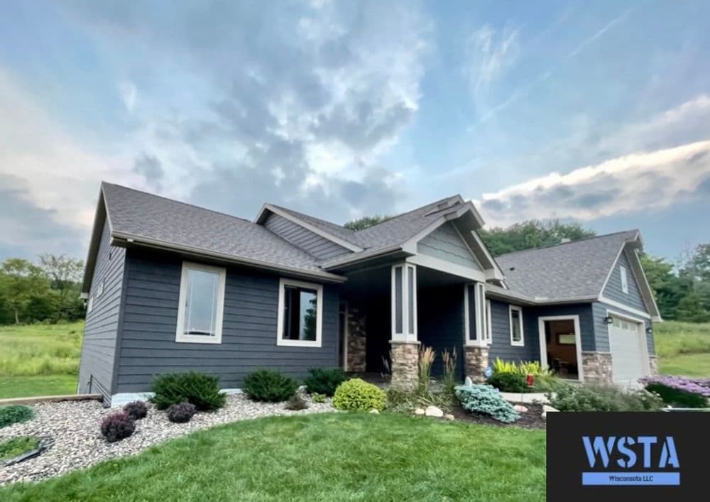 Modern gray home with stone accents and lush landscaping under a cloudy sky. WSTA logo visible.