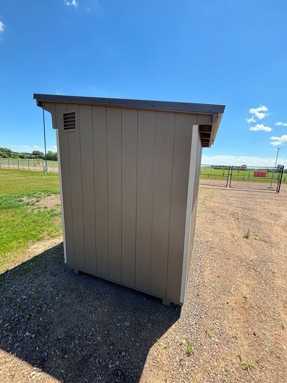 Side view of a small storage shed against a clear blue sky and grassy field.