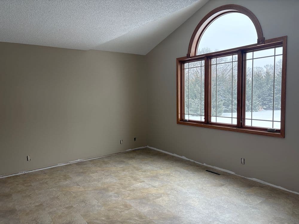 Spacious empty room with large arched window and winter landscape outside. Freshly painted walls.