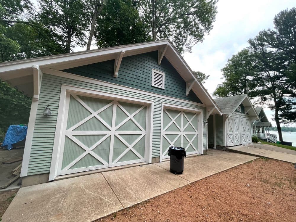 Lakeside garage with green siding and white barn-style doors on a cloudy day.