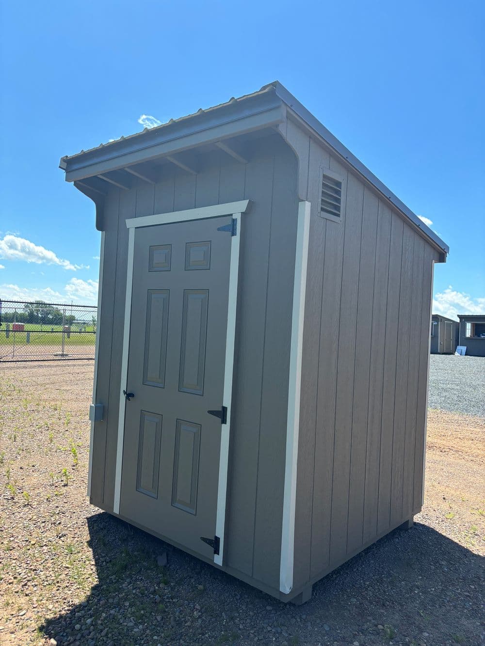 Small outdoor storage shed with a sloped roof and double doors against a clear blue sky.