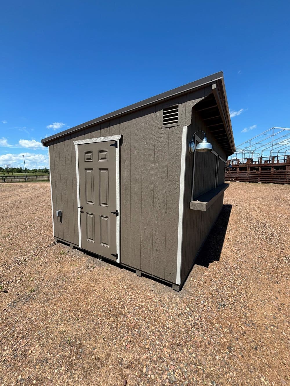 Side view of a brown storage shed with a door and window against a blue sky.