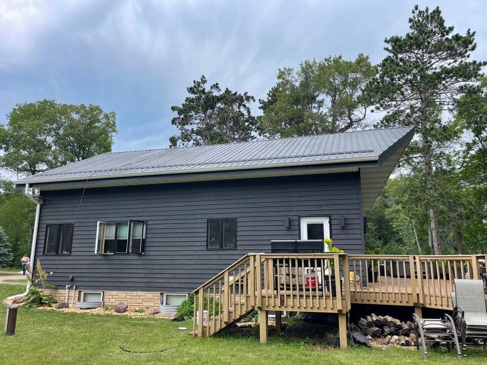 Modern dark blue house with a metal roof and wooden deck surrounded by greenery.