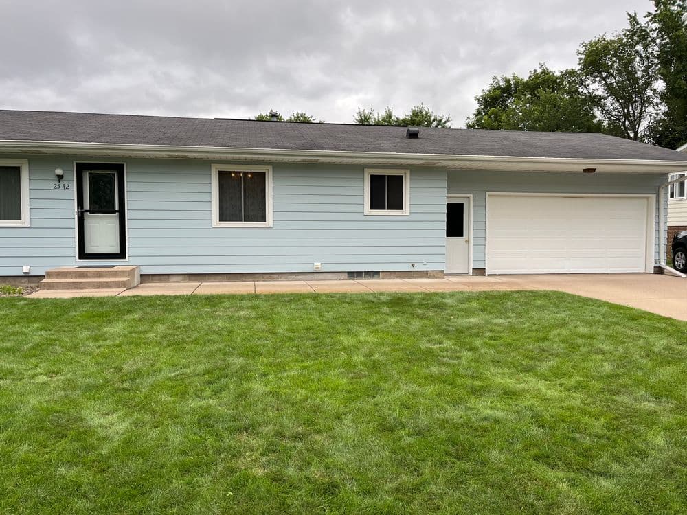 Blue single-story house with a garage and green lawn on a cloudy day.