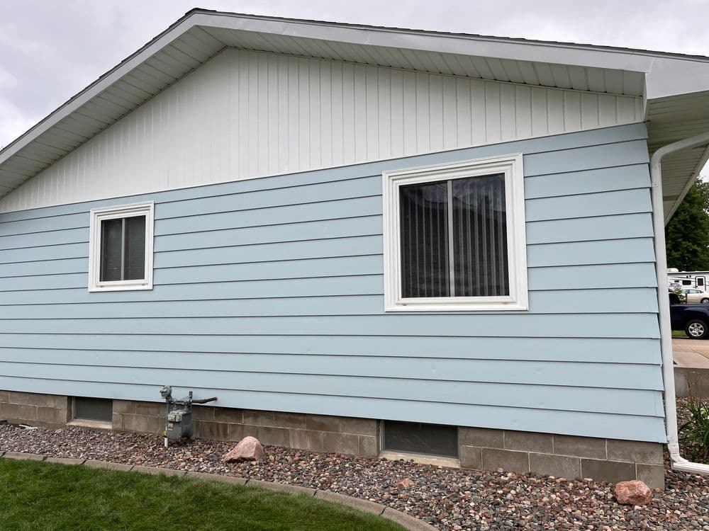 Light blue house exterior with white trim, two windows, and stone landscaping elements.