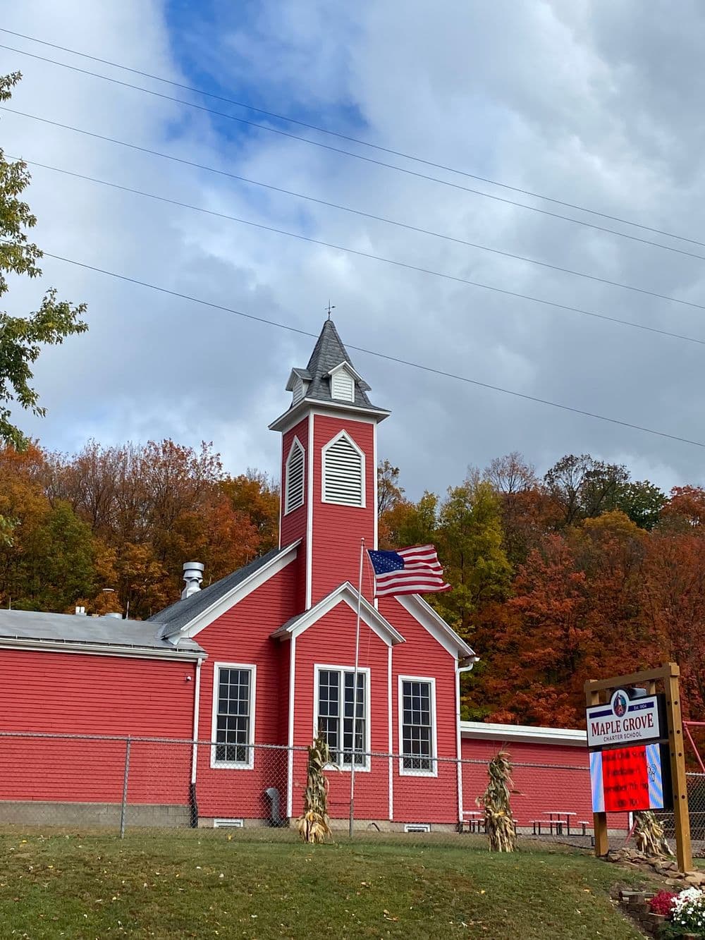 Red church building with a steeple, American flag, and colorful autumn trees in the background.