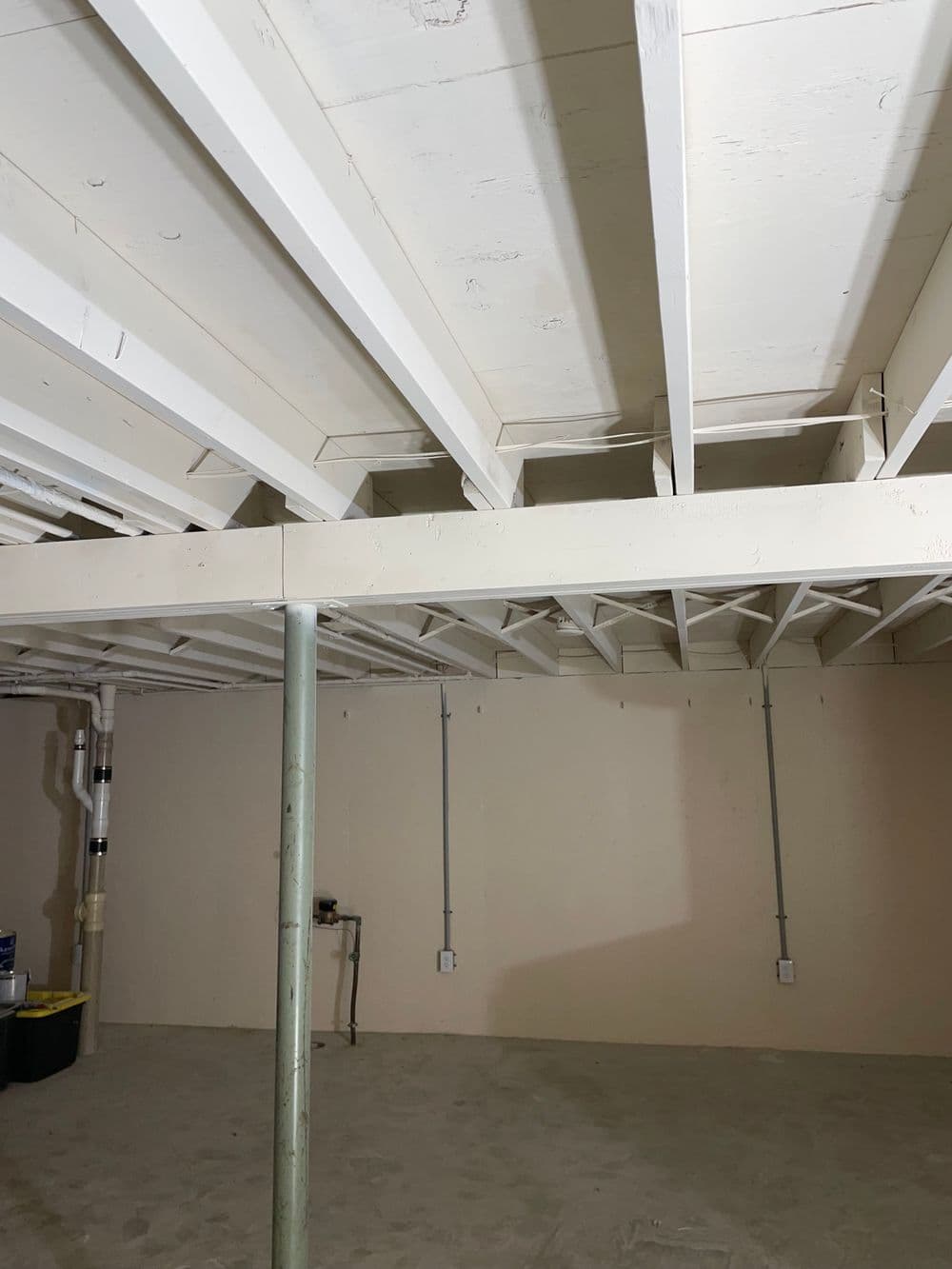 Finished basement interior with exposed beams, clear walls, and concrete floor.