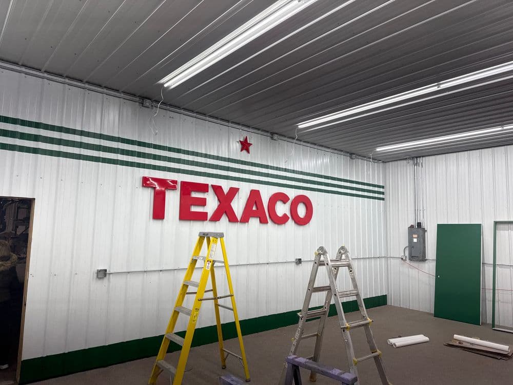 Texaco sign on a white metal wall with green stripes and ladders in a well-lit space.