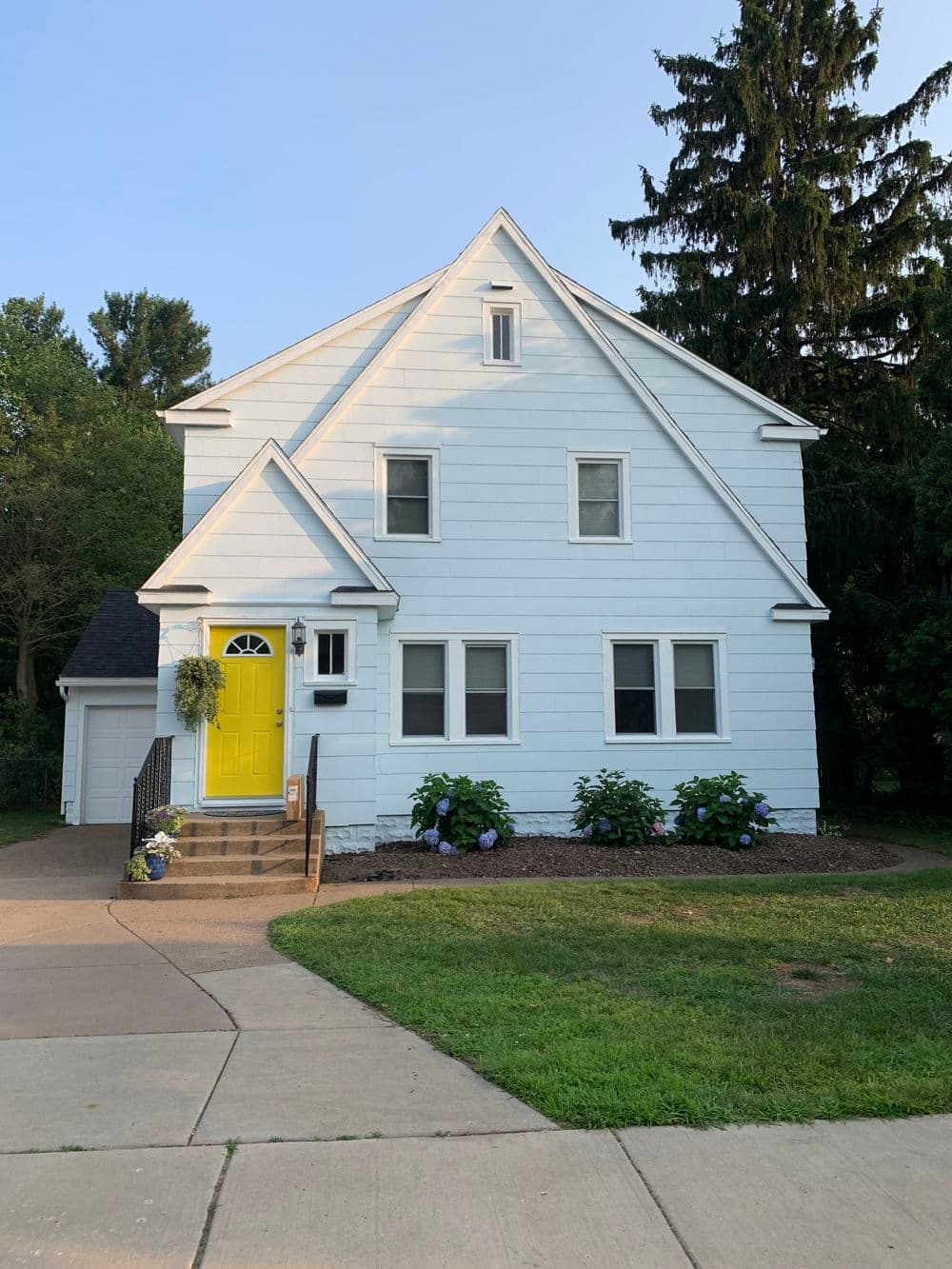 Charming light blue two-story house with yellow door and lush front garden.