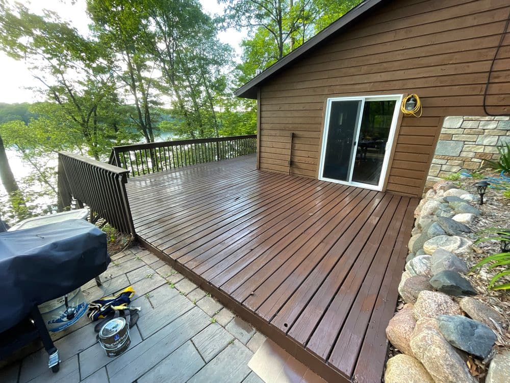 Wooden deck with a lake view, surrounded by trees, and a grill nearby. Perfect for outdoor relaxation.