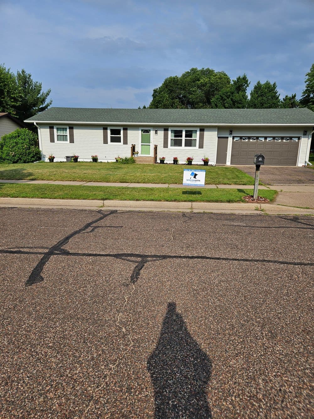 Front view of a single-story house with green door and lawn, located on a quiet street.