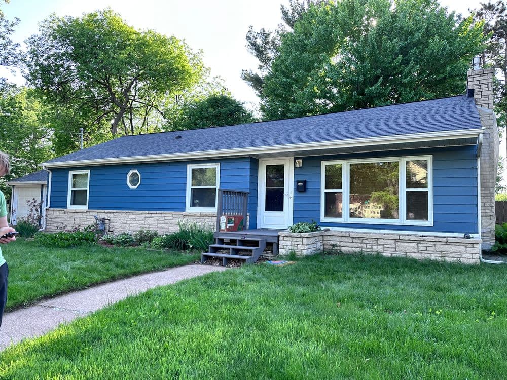 Blue ranch-style home with a stone foundation and landscaped front yard. Sunlit exterior features.
