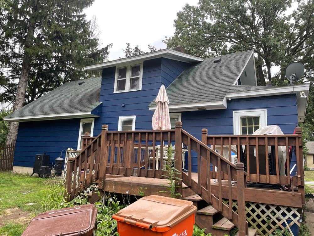 Blue house with wooden deck, patio umbrella, and backyard surrounded by trees.