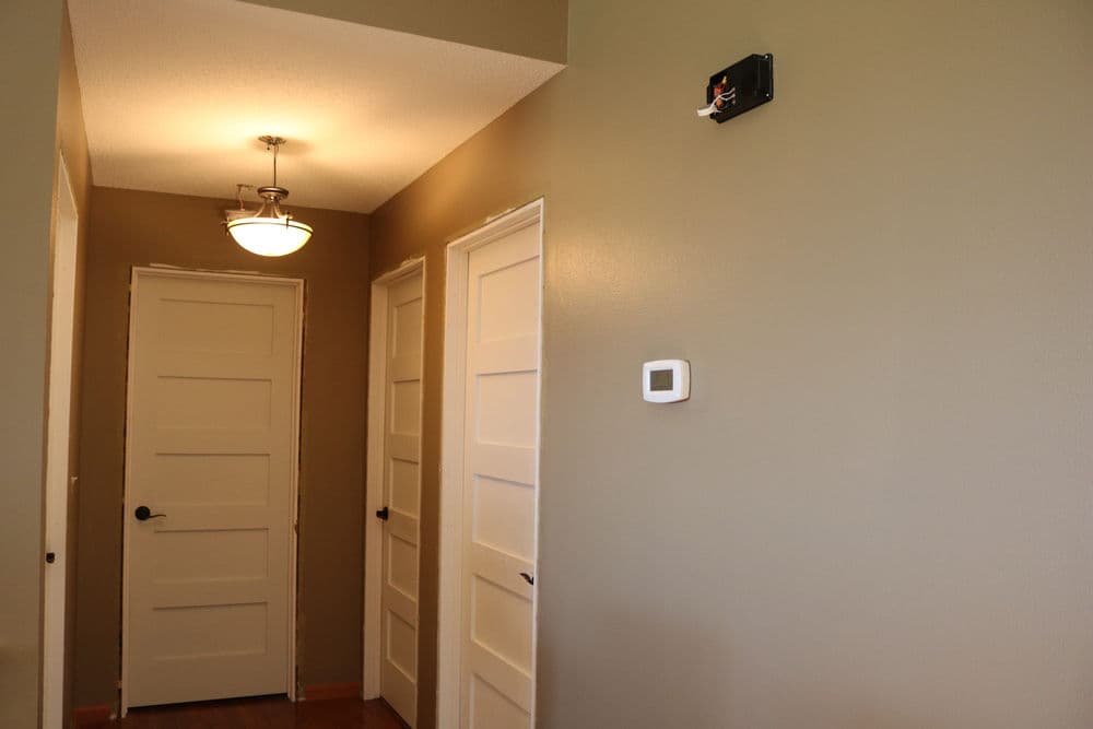 Hallway interior featuring two doors, ceiling light fixture, and a thermostat on the wall.