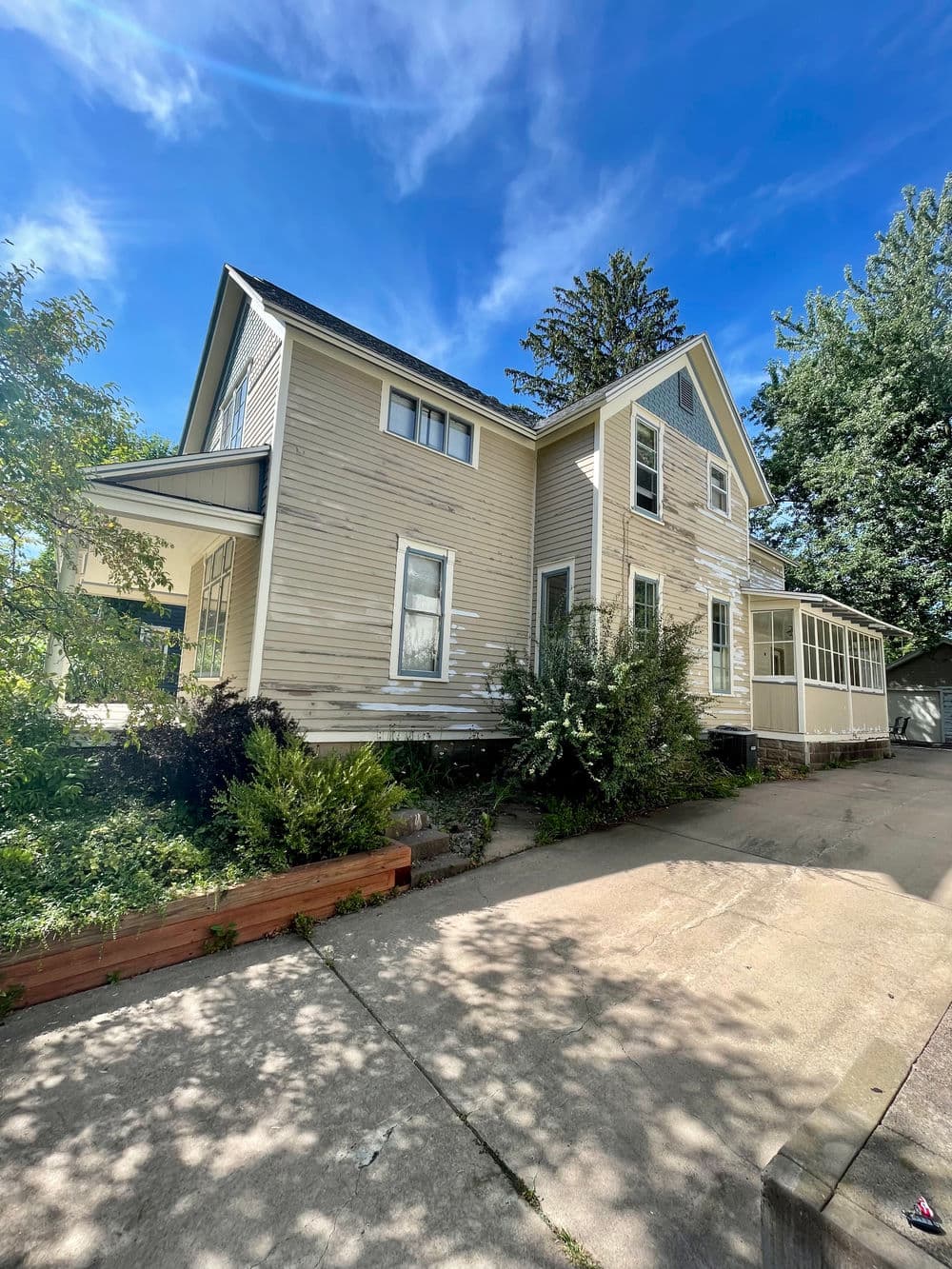 Charming two-story house with porch, surrounded by greenery and blue sky.