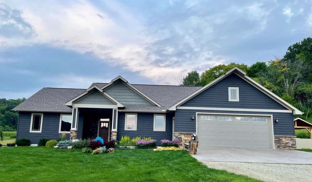 Modern blue-gray house with stone accents, lush landscaping, and a garage in a scenic setting.