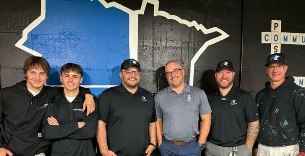 Group of five men in branded apparel smiling, standing against a Minnesota-themed backdrop.